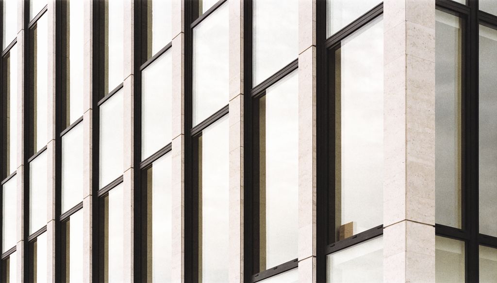 Detalhe da fachada de um edifício corporativo em vidro e pedra clara
